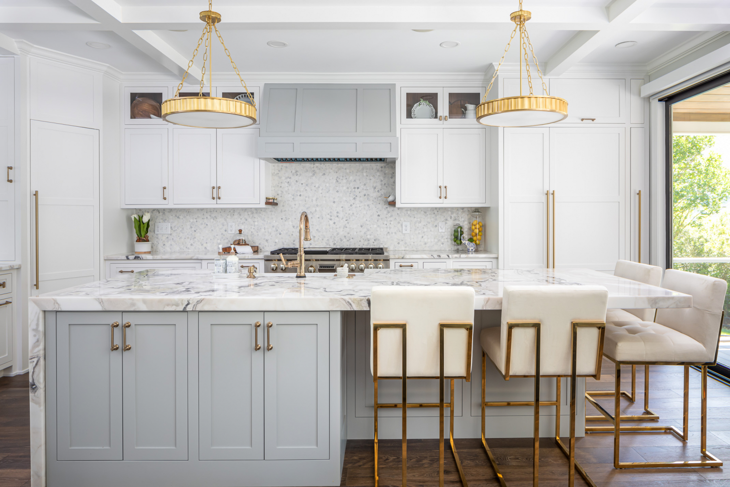 Luxury kitchen remodel with a large marble waterfall island, soft gray and white shaker cabinets, brass pendant lighting, integrated appliances, and elegant gold accents that create a bright, upscale gathering space.