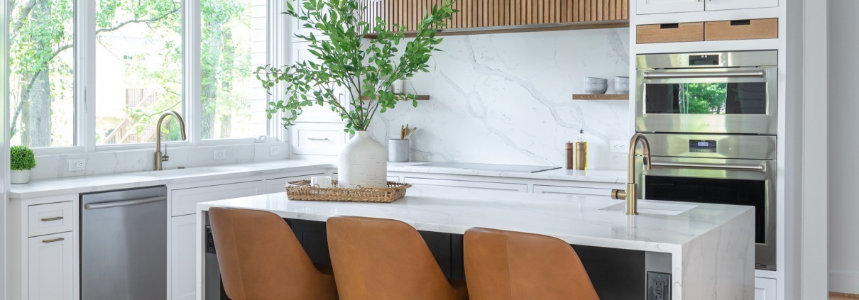 Modern kitchen remodel with a white waterfall island, black cabinetry painted sherwin williams black fox, warm wood slat custom vent hood with marble backsplash, brass fixtures, and leather barstools, creating a bright and contemporary space filled with natural light.