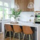 Modern kitchen remodel with a white waterfall island, black cabinetry painted sherwin williams black fox, warm wood slat custom vent hood with marble backsplash, brass fixtures, and leather barstools, creating a bright and contemporary space filled with natural light.