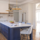 Bright transitional kitchen featuring a navy island, white cabinetry, quartz countertops, brass pendant lighting, warm wood shelving, and a layered tray ceiling detail with recessed lighting.