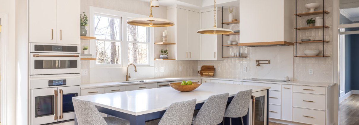 Bright transitional kitchen remodel in Raleigh NC with white custom cabinetry, navy blue island, brass pendant lighting, open shelving, and warm hardwood floors in an airy open-concept design.