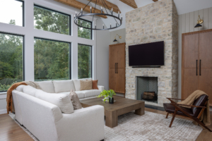 Clearcut & Co. living room remodel vaulted ceiling with exposed wood beams, large black-framed windows, black ring chandelier, and floor-to-ceiling stone fireplace.