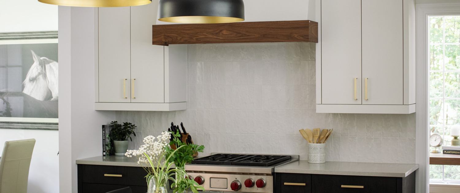 a_9 Modern kitchen with two-tone black and white cabinetry, a dark stone island, brass hardware, black and gold pendant lights, and a warm wood range hood accent.