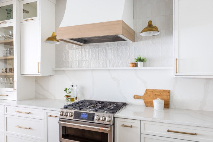 Bright white transitional kitchen remodel in Raleigh NC with waterfall island, brass pendant lighting, custom range hood, glass-front cabinetry, and warm wood accents for a timeless luxury design.