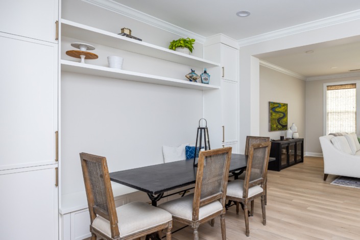 Open dining nook with built-in bench seating, custom floating shelves, and seamless flow into the adjacent living space, finished with light wood flooring and clean transitional details.