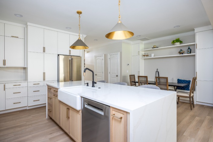 Bright transitional kitchen remodel in Raleigh NC with a large waterfall island, farmhouse sink, white shaker cabinetry, brass pendant lighting, and warm wood accents, featuring hidden appliance storage for a clean and organized design.