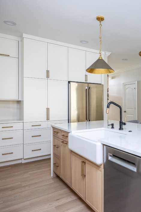Bright transitional kitchen remodel in Raleigh NC with a large waterfall island, farmhouse sink, white shaker cabinetry, brass pendant lighting, and warm wood accents, featuring hidden appliance storage for a clean and organized design.