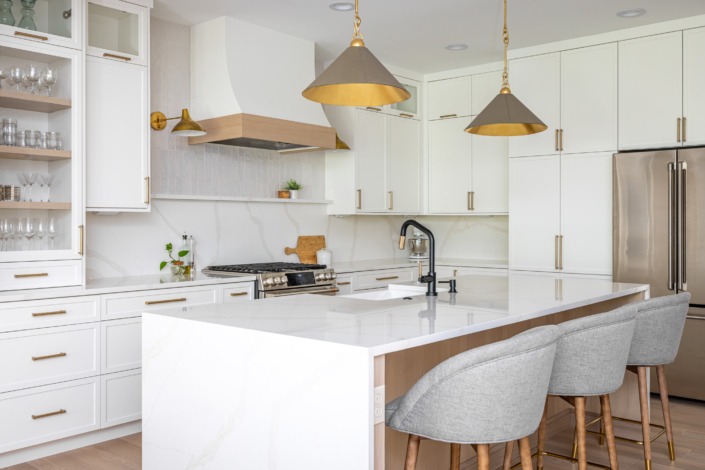 Bright white transitional kitchen remodel in Raleigh NC with waterfall island, brass pendant lighting, custom range hood, glass-front cabinetry, and warm wood accents for a timeless luxury design.
