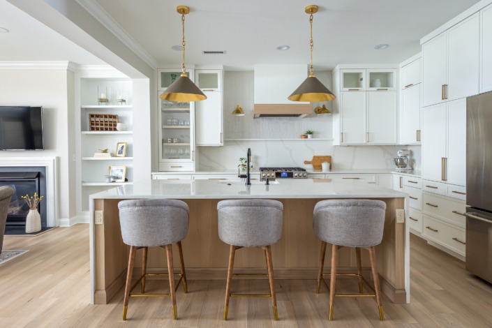 Bright transitional kitchen remodel in Raleigh NC with white custom cabinetry, warm wood island accents, brass pendant lighting, waterfall countertops, and open-concept luxury design.
