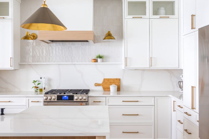 Bright white transitional kitchen remodel in Raleigh NC with waterfall island, brass pendant lighting, custom range hood, glass-front cabinetry, and warm wood accents for a timeless luxury design.