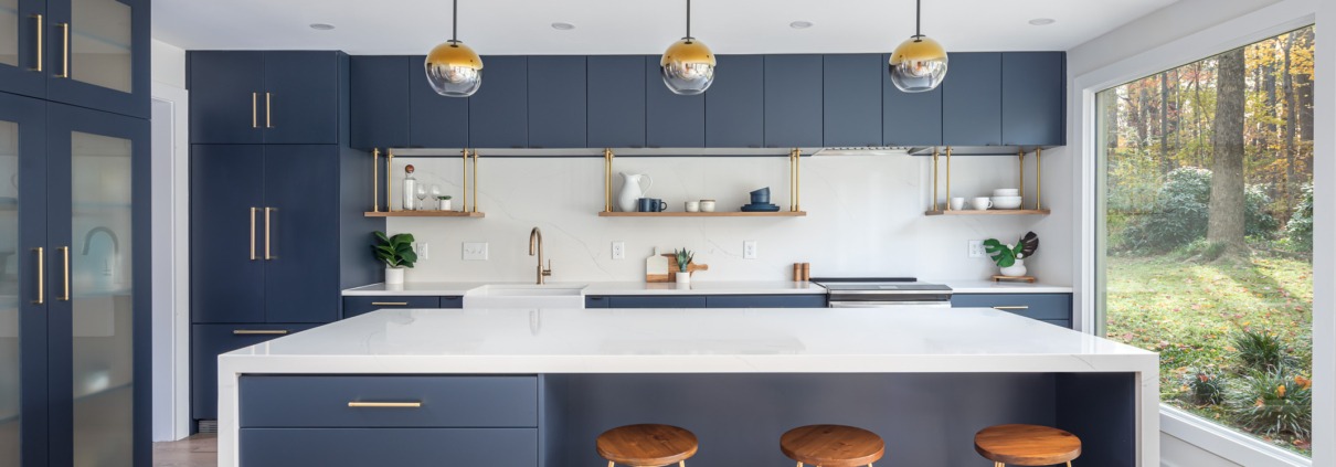 Modern kitchen with deep navy cabinets, a large white waterfall island, brass hardware, floating wood shelves, globe pendant lights, and large picture windows.
