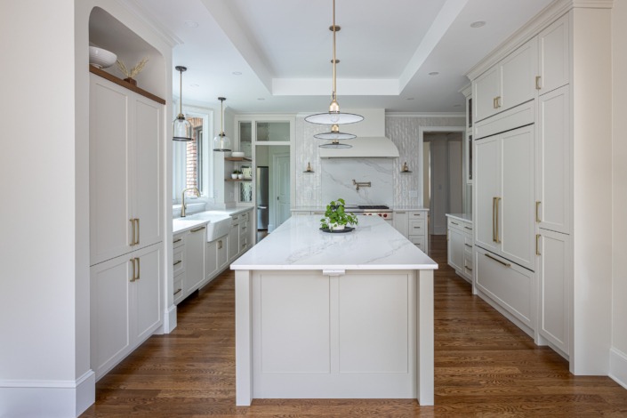 Elegant white kitchen remodel with a large quartz island, custom shaker cabinetry, brass hardware, statement pendant lighting, and warm wood flooring that create a bright, timeless, and luxurious gathering space.