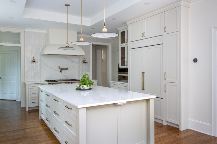 Bright transitional kitchen remodel featuring custom inset cabinetry, a large quartz island with abundant storage, brass hardware, panel ready refrigerator to match cabinets, and custom vent hood creating a refined yet welcoming design.