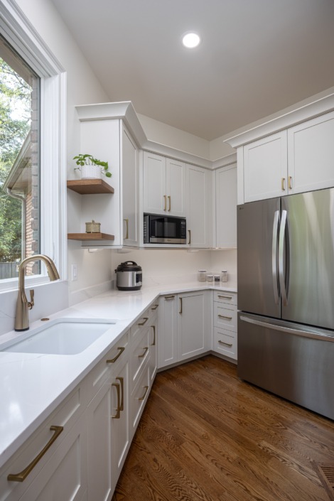 Functional walk-in pantry featuring custom white cabinetry, integrated refrigerator and microwave storage, quartz countertops, warm brass hardware, open wood shelving, and a secondary prep sink designed for seamless everyday organization and convenience.