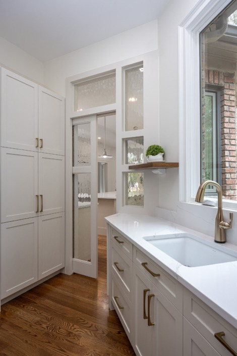 Custom pantry with floor-to-ceiling cabinetry, a secondary prep sink, warm brass fixtures and hardware, and decorative glass transom windows that create a bright, functional extension of the main kitchen.