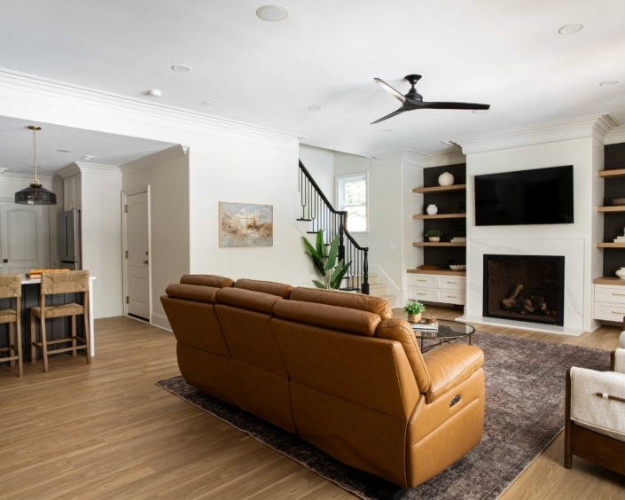 Wakefield_IMG_0004 Custom, high end basement living room with a caramel leather sofa, warm wood flooring, custom fireplace built-ins, and an open view toward the adjoining spaces.