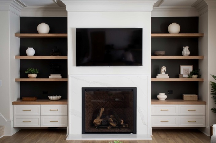 Wakefield_IMG_0013 Basement lounge featuring a modern fireplace with mounted TV, flanked by custom built-in cabinetry and warm wood floating shelves.