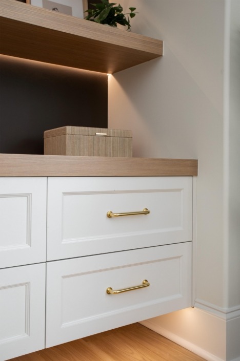 Wakefield_IMG_0019 Custom white built-in cabinetry with brass hardware, warm wood countertop, and softly lit display niche.