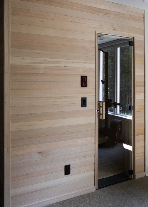 Wakefield_IMG_0024 92) Custom home sauna with warm wood-paneled walls and a glass door, located beside the basement home gym.