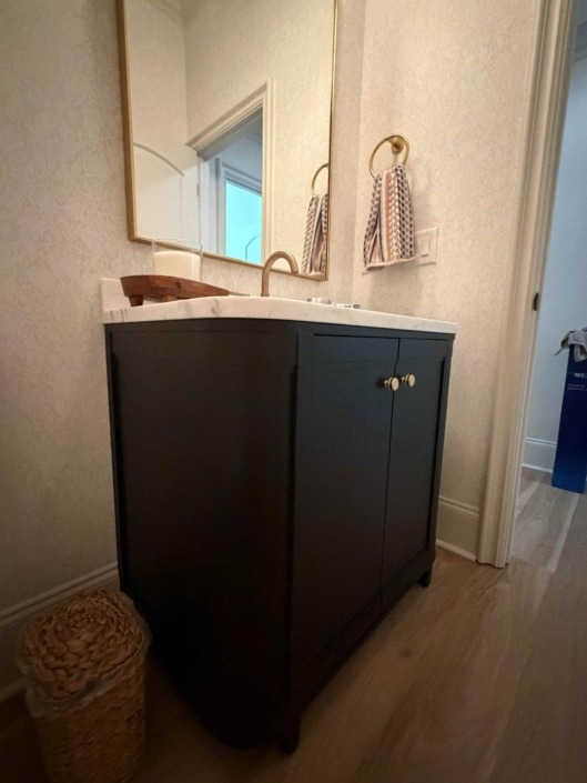 wakefield IMG_1446 Compact basement bathroom vanity with dark blue cabinetry, white countertop, brass hardware, and a modern vessel sink.