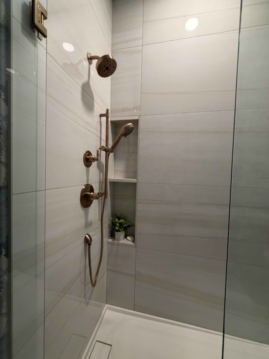 wakefield IMG_1455 Modern walk-in shower featuring large-format white tile, a frameless glass enclosure, built-in shower niche, and matte black plumbing fixtures.
