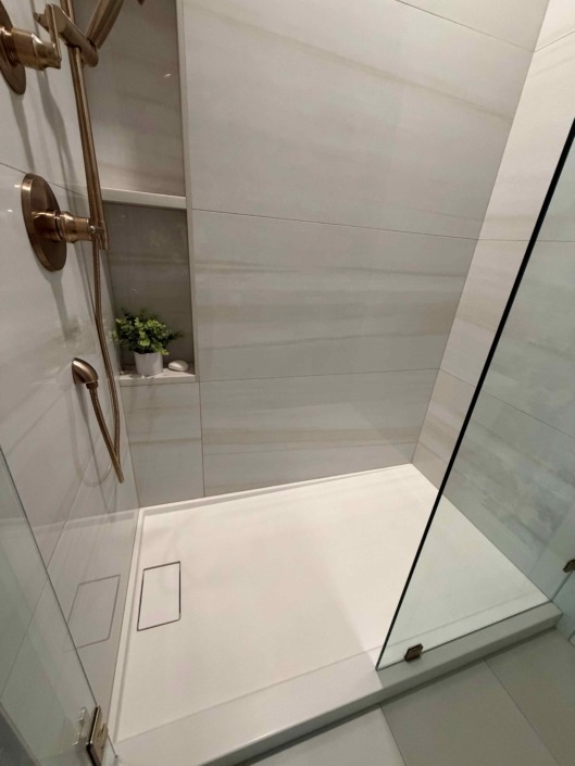 wakefield IMG_1456 Modern walk-in shower featuring large-format white tile, a frameless glass enclosure, built-in shower niche, and matte black plumbing fixtures.